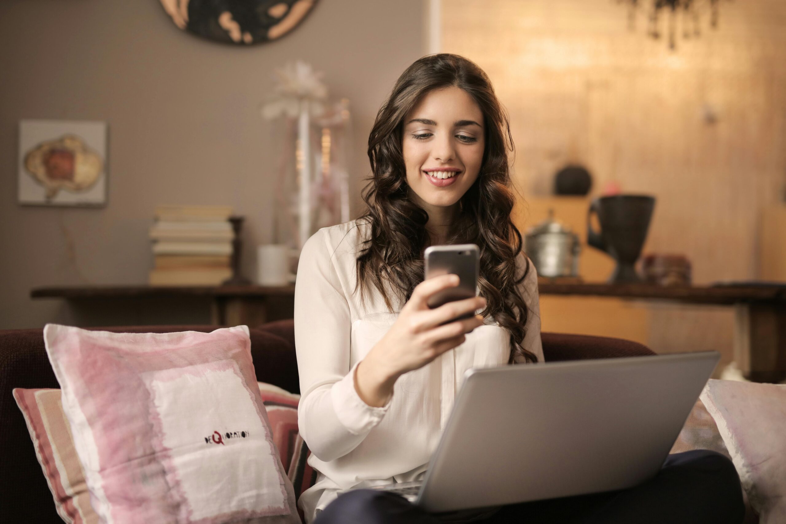 Grundlagen des Affiliate Marketings: Nischen und Strategien 2 Frau, Die Auf Sofa Sitzt, Während Telefon Mit Laptop Auf Schoß Betrachtet